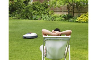 Couple qui joue a un jeu de société pendant que le robot tondeuse s'occupe de la pelouse.
